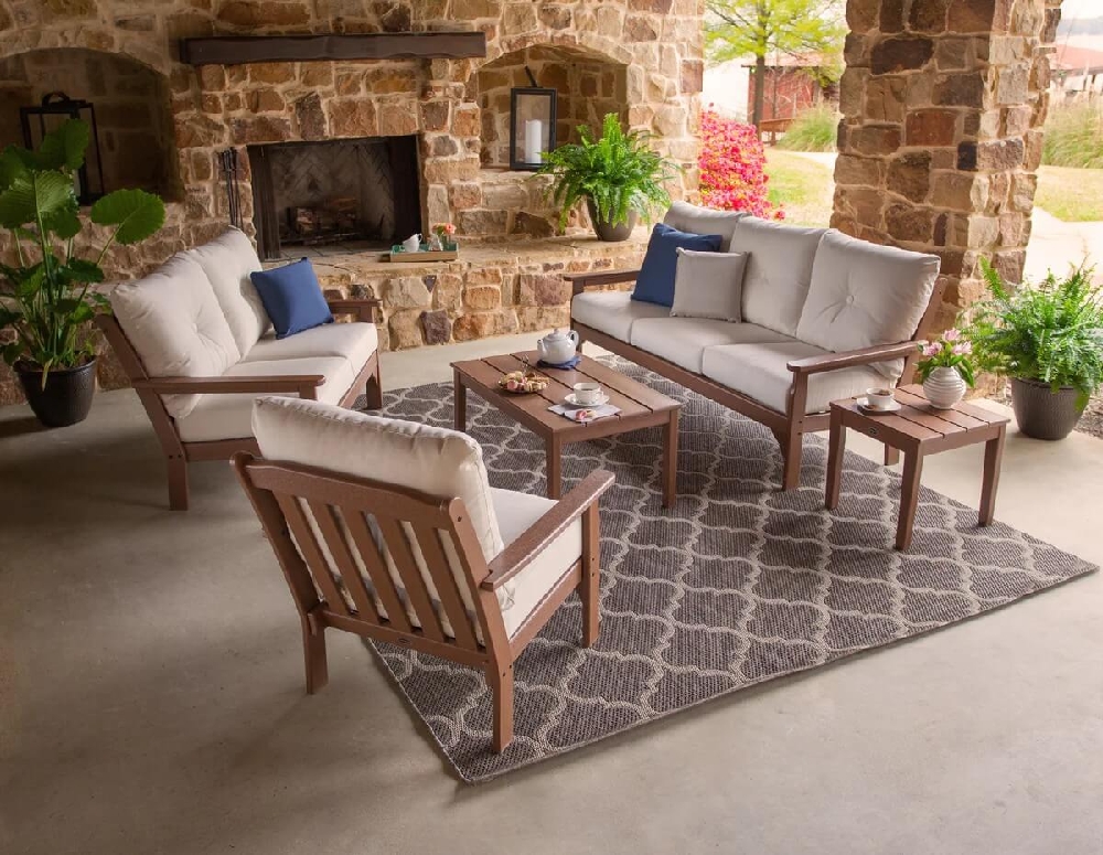 Commercial deep seating furniture arranged around a coffee table in a covered outdoor lounge with a stone fireplace.